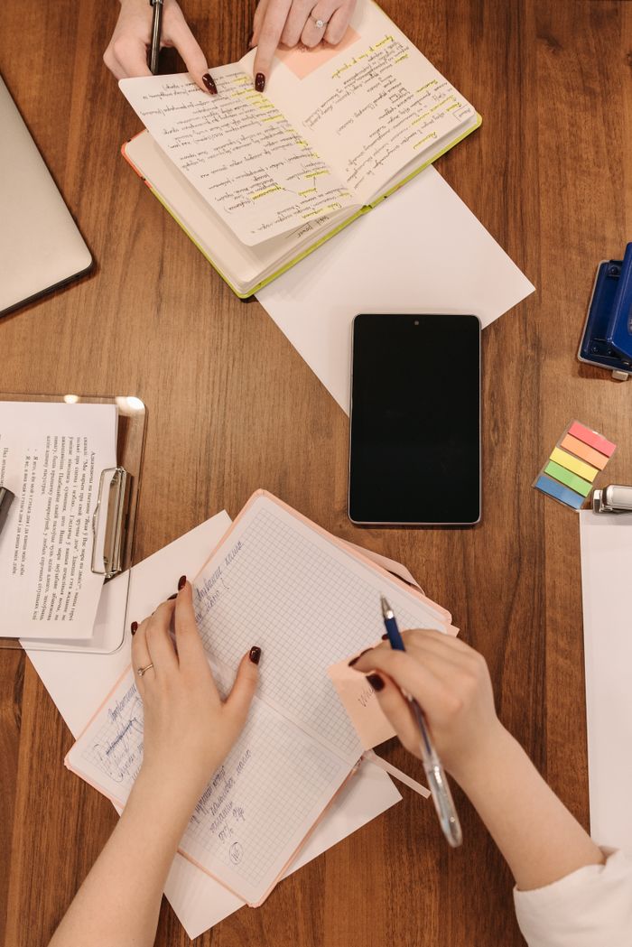 Overhead view of a collaborative meeting with notebooks and a tablet on a wooden table.