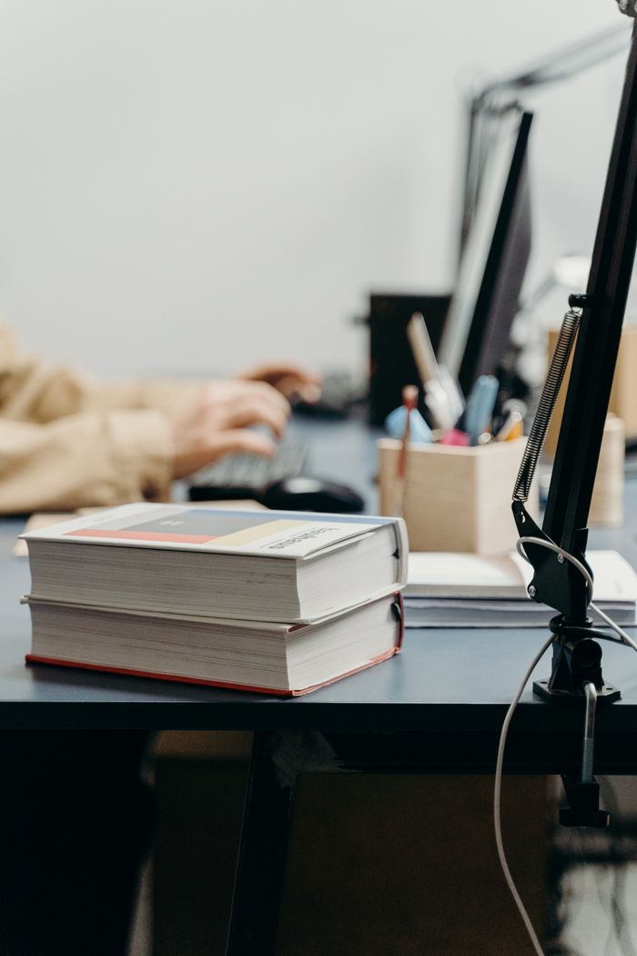 A warm workspace with books, computer, and person working, perfect for studying or remote work.